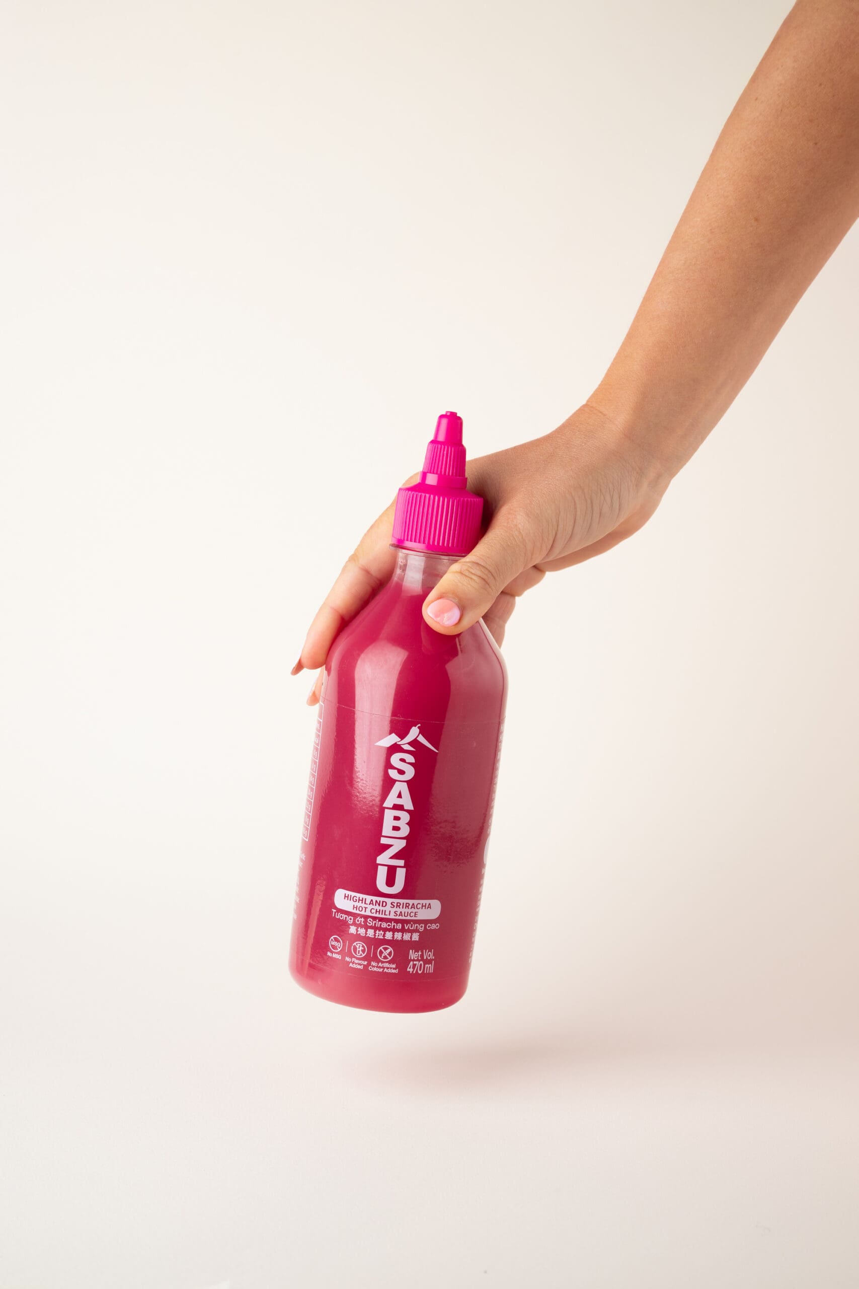 A hand holding a bright pink squeeze bottle labeled "SABZU" against a plain white background.