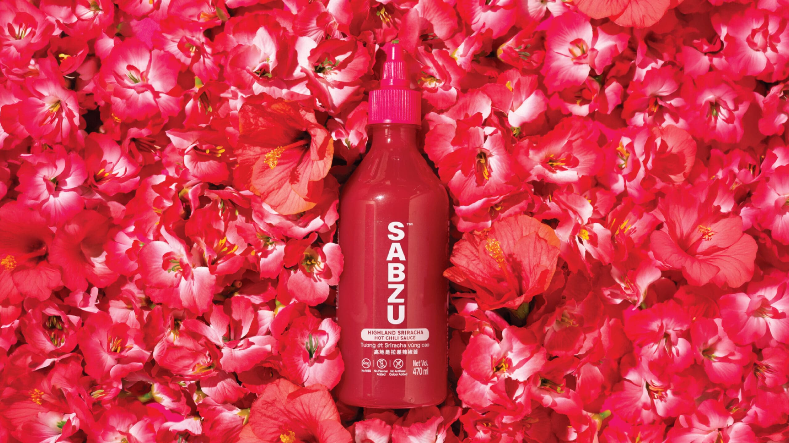 A red bottle labeled "SABZU" sits on a bed of vibrant pink and red flower petals, creating a bright and colorful composition.