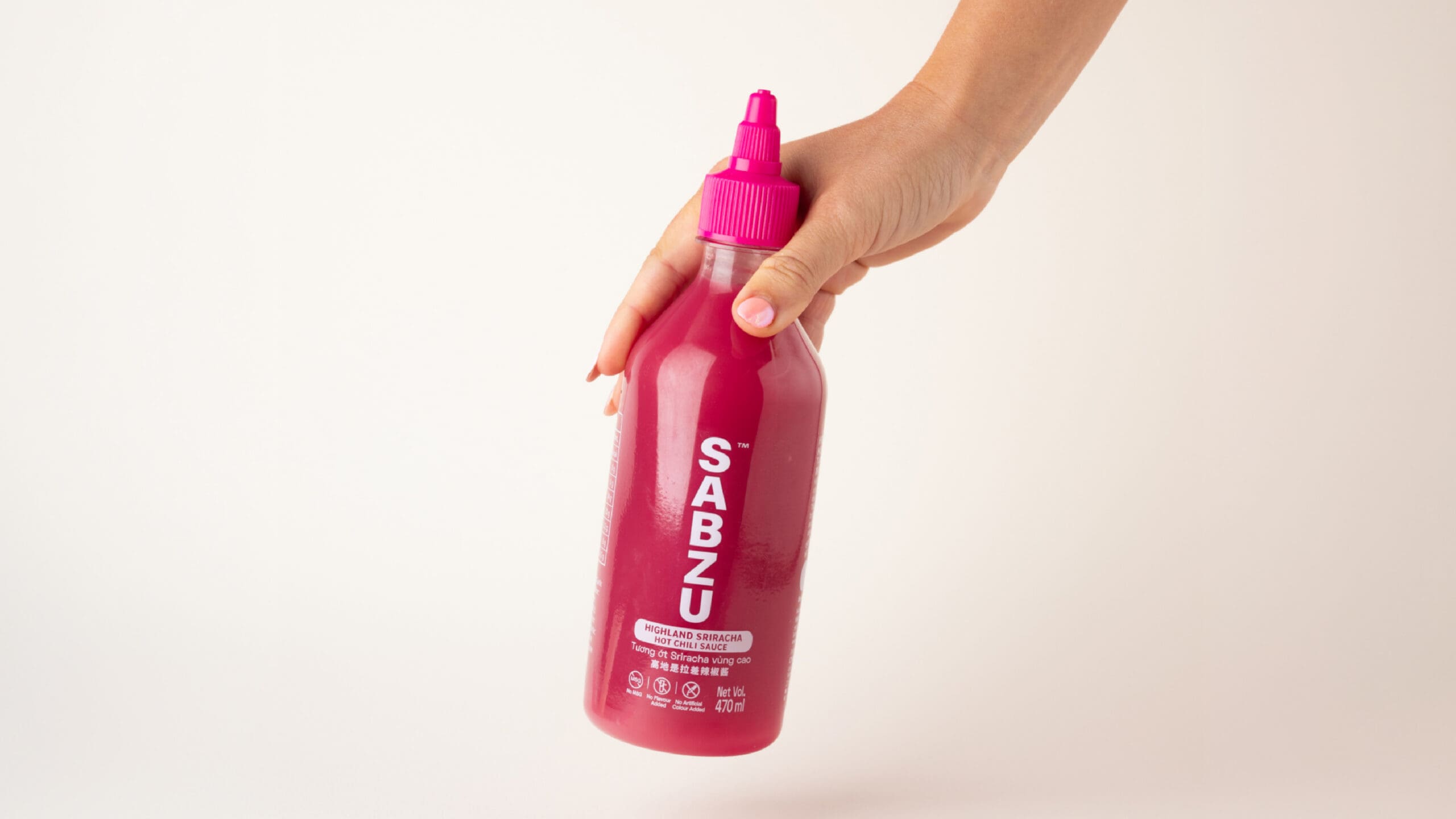 A hand holds a pink squeeze bottle labeled "SABZU" with a spout cap against a plain white background.